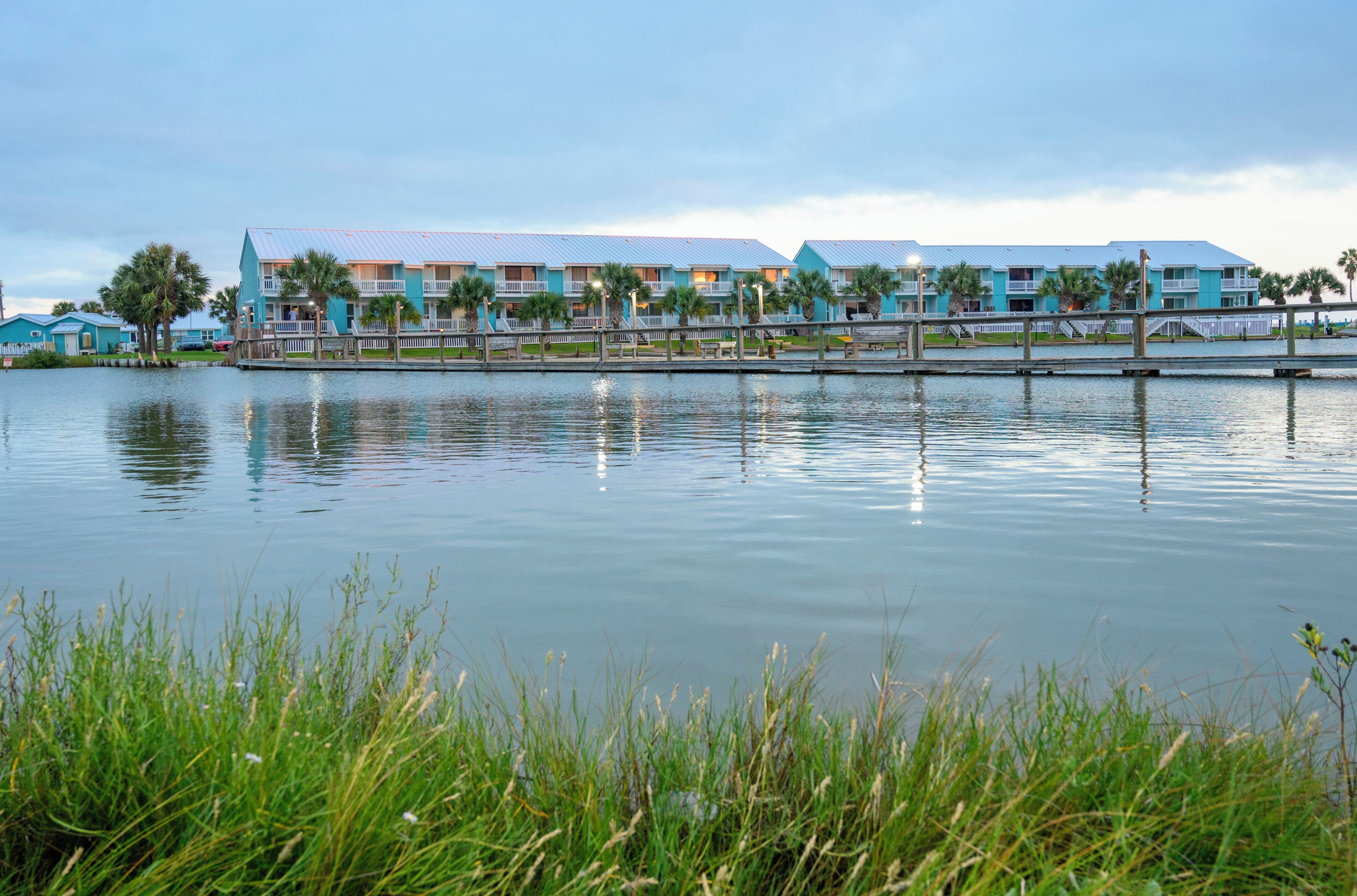 Hotel amb vistes al mar, diversos balcons, un moll i un llac tranquil.