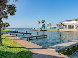 Um imóvel à beira-mar com um cais, um edifício com telhado azul e uma área ajardinada.