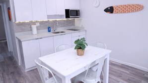 A compact kitchen with white cabinets, a microwave, a sink, and a dining area with a table and chairs. - 1111 Douglas · Remodeled 1bed/1bath apt w/parking great location (Miami)