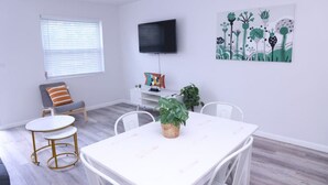 A modern living room with a white table, chairs, a TV, and a painting. - 1111 Douglas · Remodeled 1bed/1bath apt w/parking great location (Miami)
