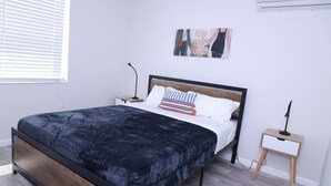 A modern bedroom with a bed, bedside tables, and a wall-mounted air conditioner. - 1111 Douglas · Remodeled 1bed/1bath apt w/parking great location (Miami)