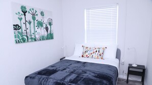 A bedroom with a bed, a nightstand, a bedside lamp, a window with blinds, and a wall art piece. - 1113 Douglas rd · Cozy Studio w/ parking & private patio w/ BBQ (Miami)