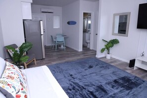 Quarto moderno com uma cama, uma escrivaninha e uma cadeira. Há uma pequena mesa com uma planta e uma cadeira azul. O quarto tem paredes brancas e piso cinzento.