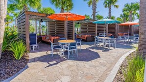 An outdoor patio area with wooden seating, tables, and umbrellas. - Paradise Resort (Davenport)