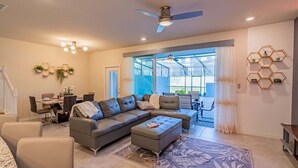 A modern living room with a sectional sofa, a dining area, and a large window with a view. - Paradise Resort (Davenport)