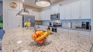 A kitchen with white cabinets, a granite countertop, a microwave, and a fruit bowl. - Paradise Resort (Davenport)