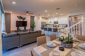 A modern living room with a sofa, dining table set for four, and a kitchen in the background. - Paradise Resort (Davenport)