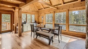 L’intérieur d’un chalet en bois comprend un coin repas, de grandes fenêtres et une vue sur la forêt.