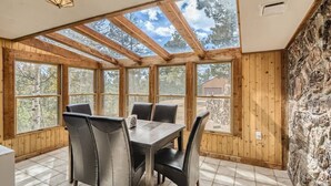 Un espace repas comprenant une table et des chaises, de grandes fenêtres, des poutres en bois et un mur en pierre.