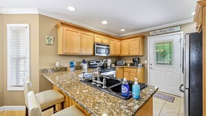 A kitchen with wooden cabinets, granite countertops, a stainless steel sink, a microwave, and a refrigerator.