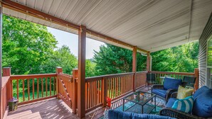 A covered outdoor deck with wooden railings, wicker furniture, and a view of lush greenery.