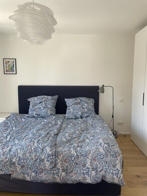 Ett sovrum med en säng, en sänggavel, en sänglampa och en väggmonterad lampa.