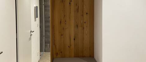 A room with a wooden wardrobe, a bench, and a door leading to another room.