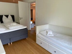 Habitación de hotel con dos camas, suelo de madera y puerta que da a un baño.