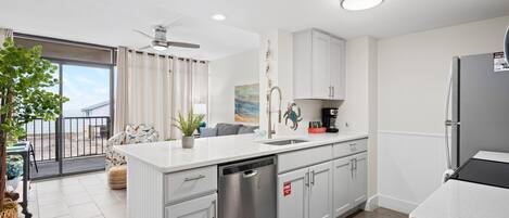 A modern kitchen with white cabinetry, a dishwasher, and a refrigerator. There is a dining area with a table and chairs, and a balcony with a view.