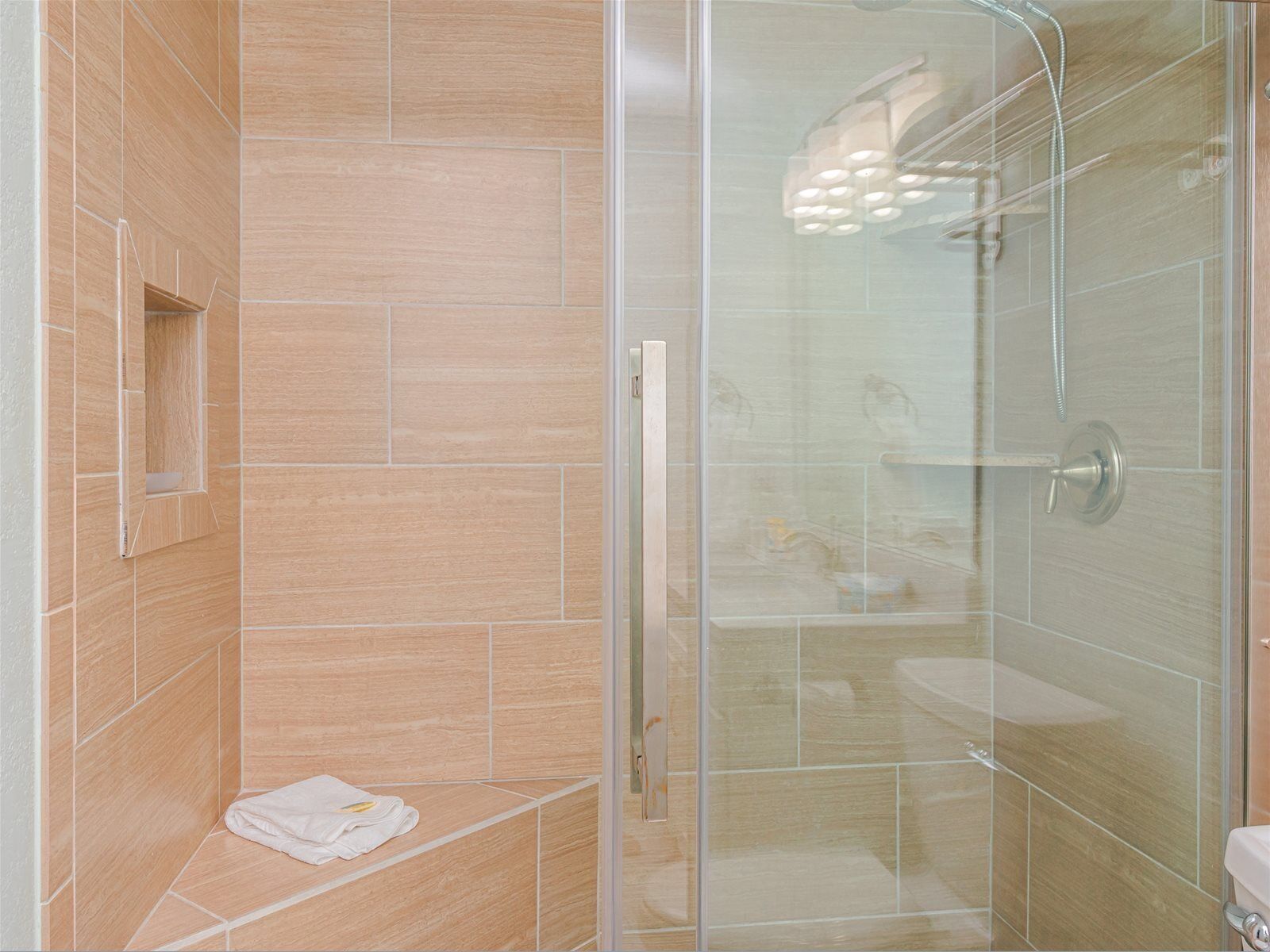 Une douche fermée par des parois de verre, avec une porte en verre, un porte-serviettes et une petite étagère.