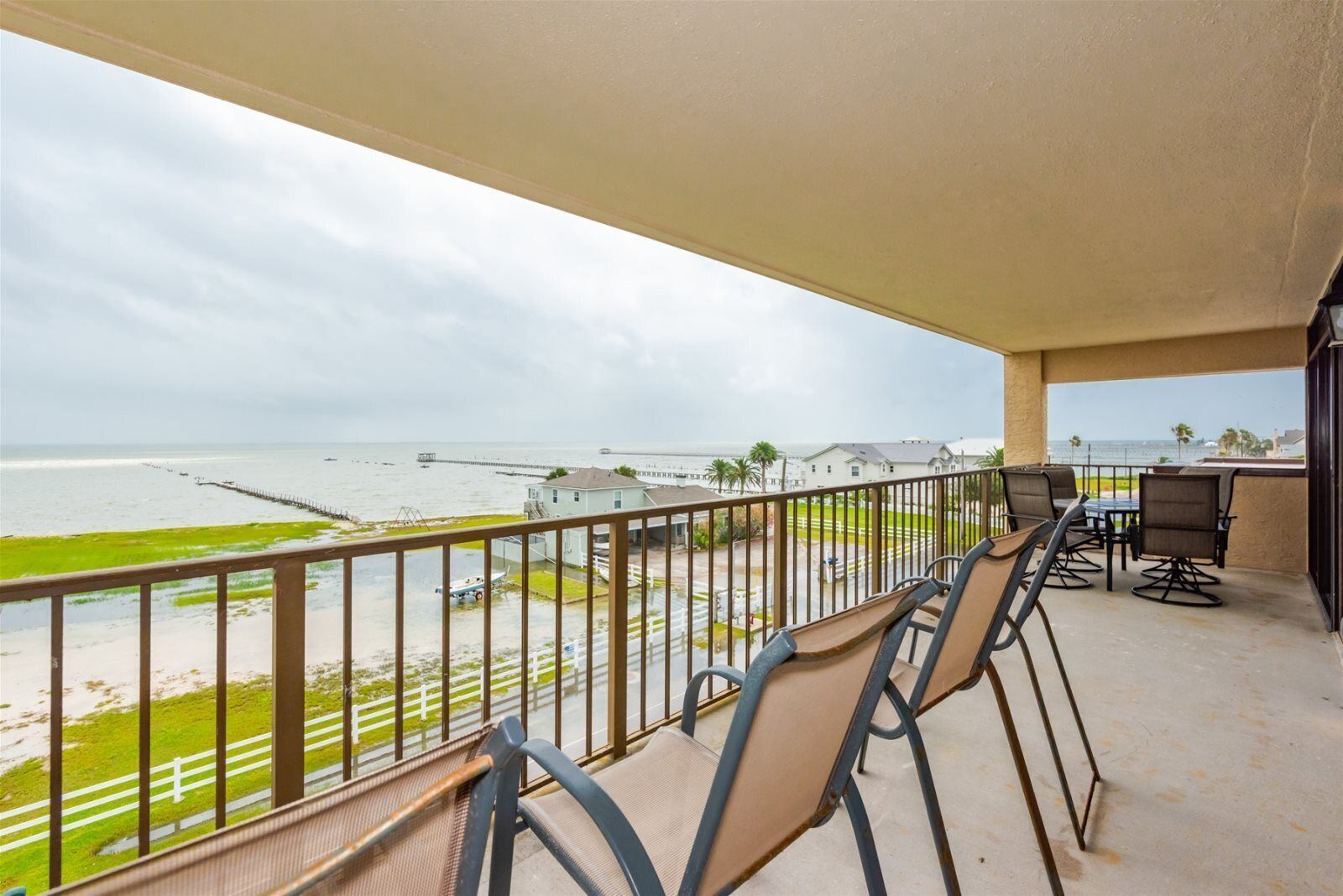 A balcony with chairs and a table overlooking a beach and ocean.