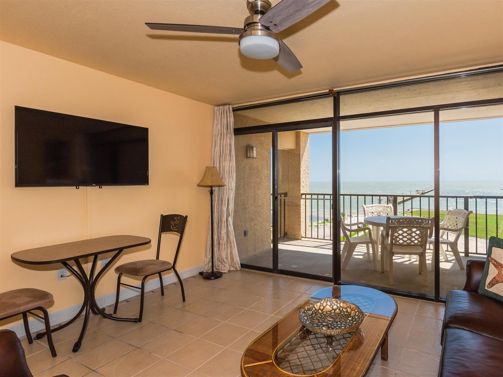 Une pièce comprenant une télévision, une table, des chaises, un canapé, un vase décoratif et un balcon avec vue sur la mer.