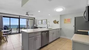 A modern kitchen with a large island, a dishwasher, and a view of the sea. - Laguna Reef 2 by Miss Kitty’s (Rockport)