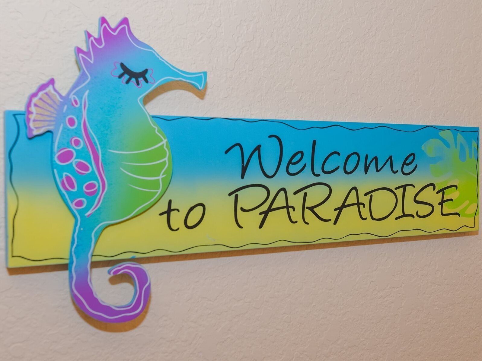 Een kleurrijk zeepaard-bord met de tekst 'Welcome to PARADISE'.