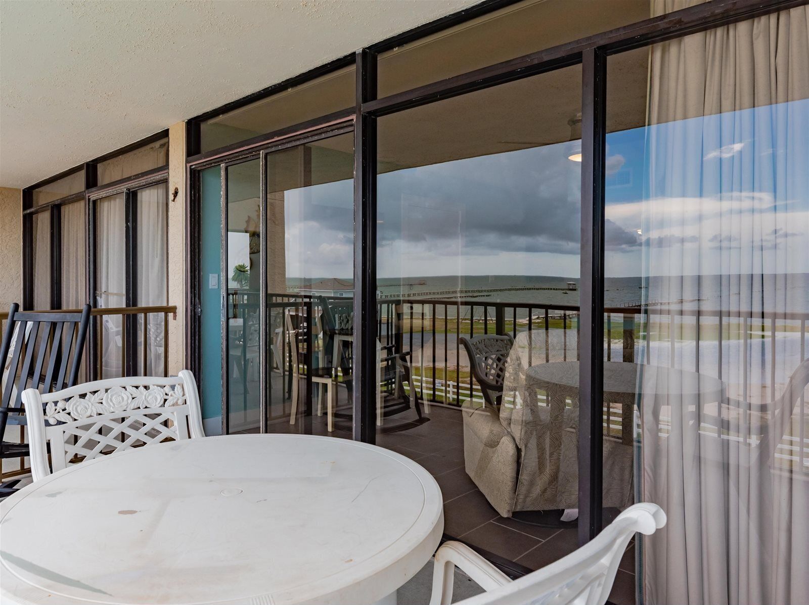 A balcony with a table and chairs, offering a view of the sea and a distant bridge.