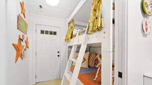 Un lit superposé pour enfants avec une échelle, une porte blanche et des décorations en forme d’étoiles sur le mur.