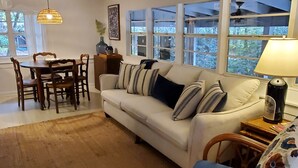 Un salon comprenant un canapé, une table basse, une table à manger avec des chaises, et une grande fenêtre à plusieurs vitres.
