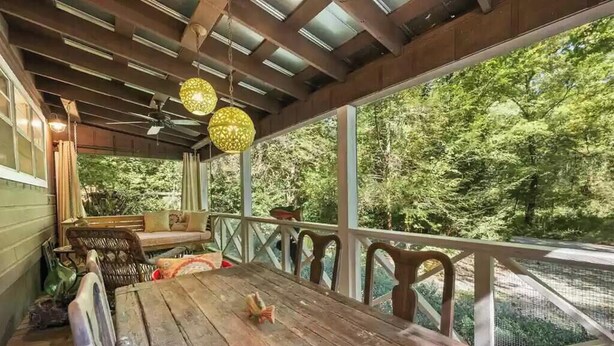Un espace extérieur abrité, doté d’une table et de chaises en bois, d’un banc et de lampes sphériques suspendues.