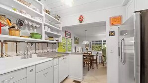 Une cuisine avec des meubles blancs, un réfrigérateur en acier inoxydable et un coin repas avec des chaises en bois.