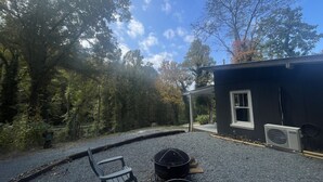 Un patio de grava con una parrilla negra, una silla y un pequeño edificio con un equipo de aire acondicionado.