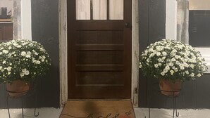 Puerta principal con un adorno de corona, felpudo y dos macetas a cada lado.