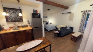 Una habitación compacta con kitchenette, una cama, un sofá y una pequeña mesa.