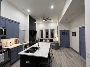 A modern kitchen with a central island, built-in appliances, and a dining area with a gray sofa.