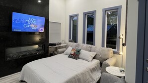Un dormitorio moderno con una cama, un televisor, un ventilador de techo y un pequeño rincón de descanso.