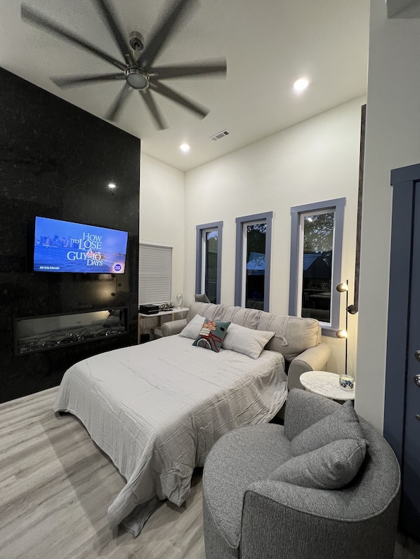 A modern bedroom with a bed, a TV, a ceiling fan, and a small seating area.