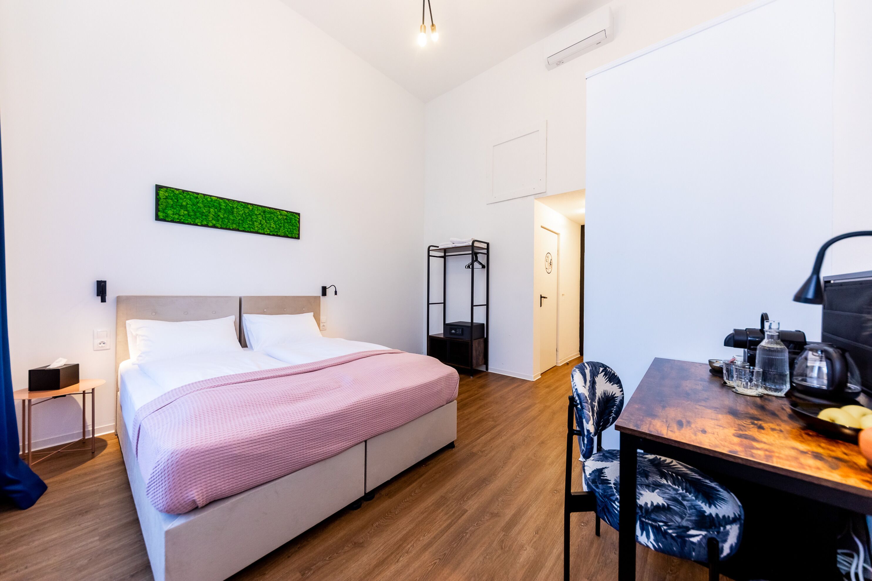 Habitació d'hotel moderna amb un llit gran, una taula de treball amb una cadira i una taula petita amb una làmpada.