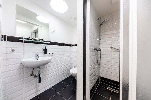 A modern bathroom with a white sink, black-tiled floor, a toilet, and a glass-enclosed shower area.