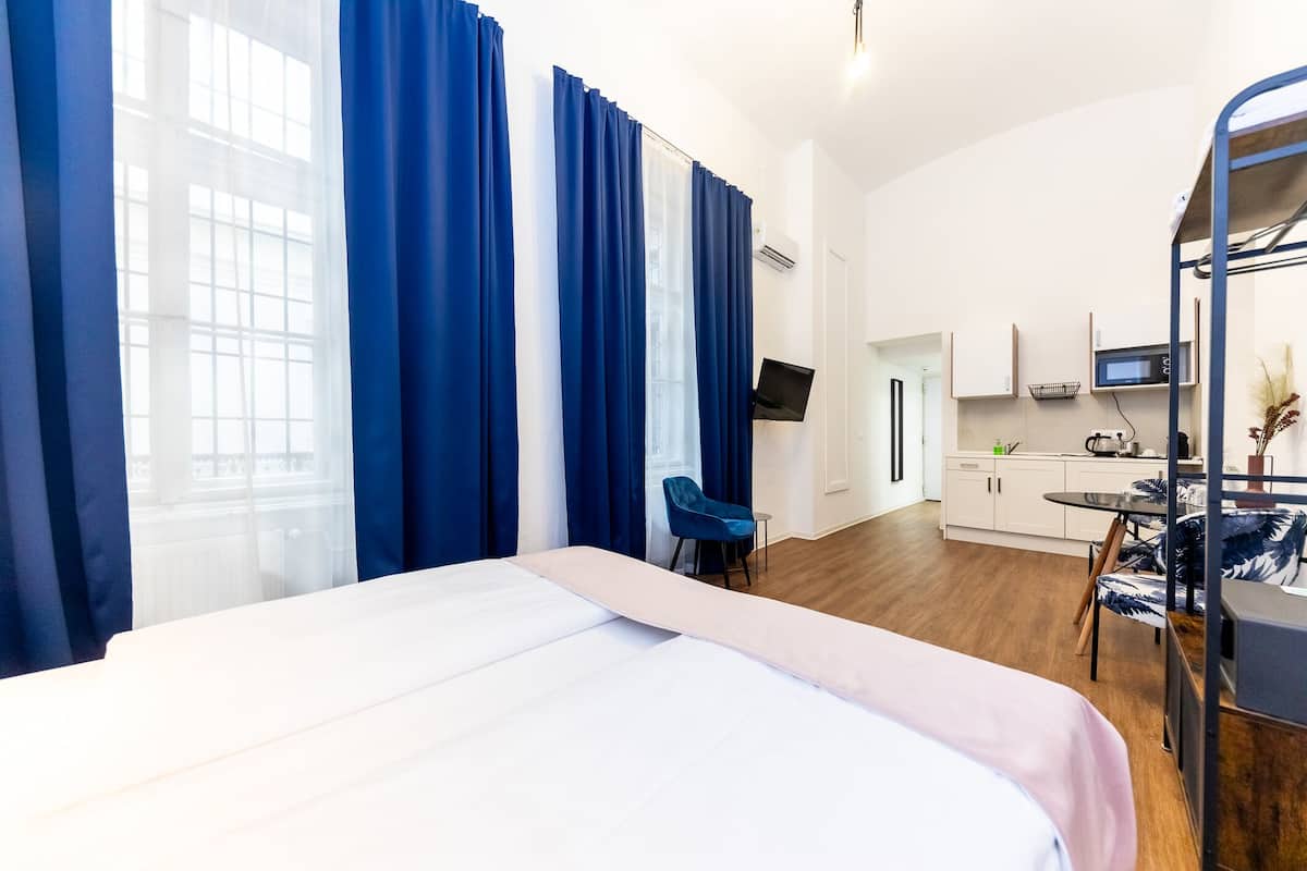 A hotel room with a bed, a desk, a chair, a TV, and a kitchenette.