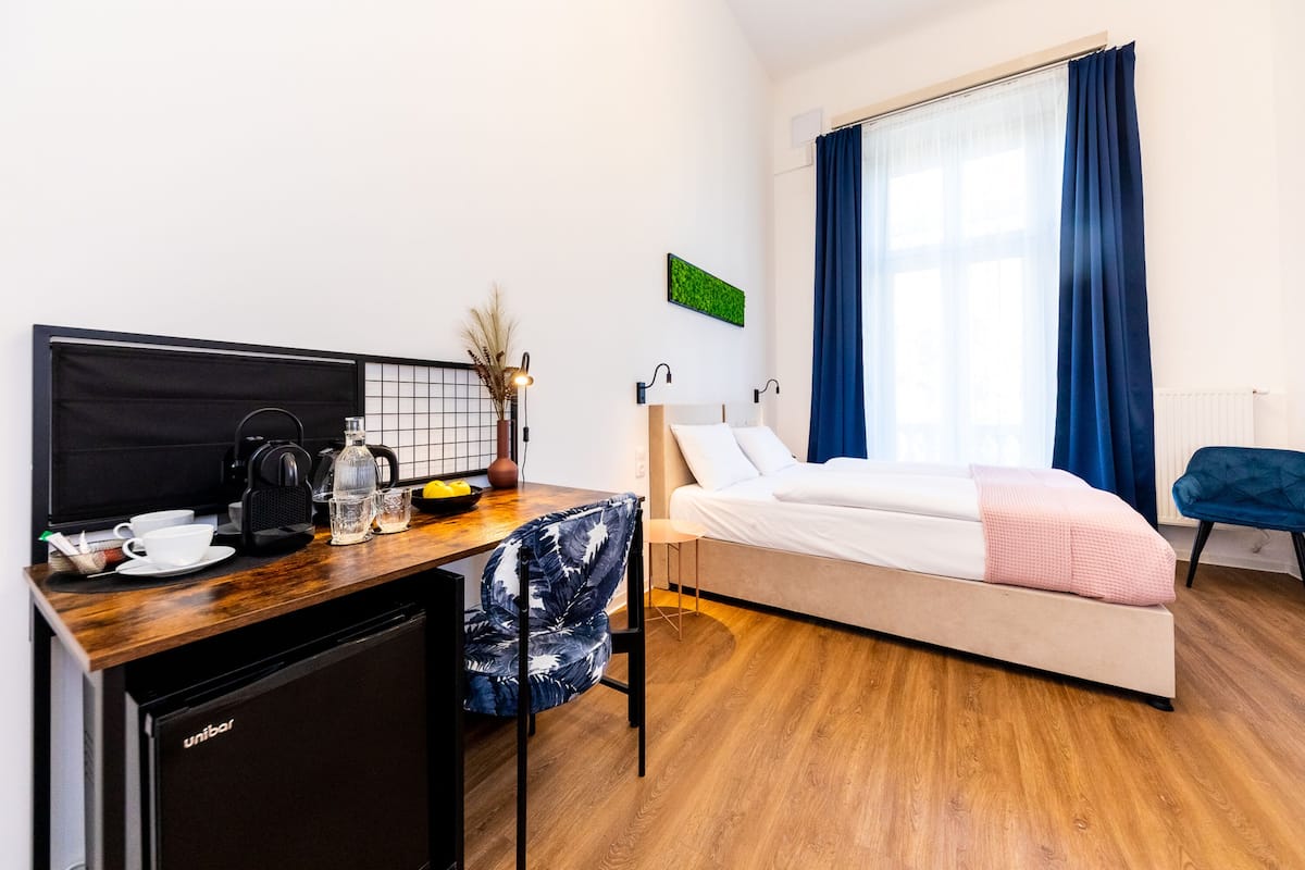 A hotel room with a bed, a desk with a computer, a coffee maker, and a small refrigerator.