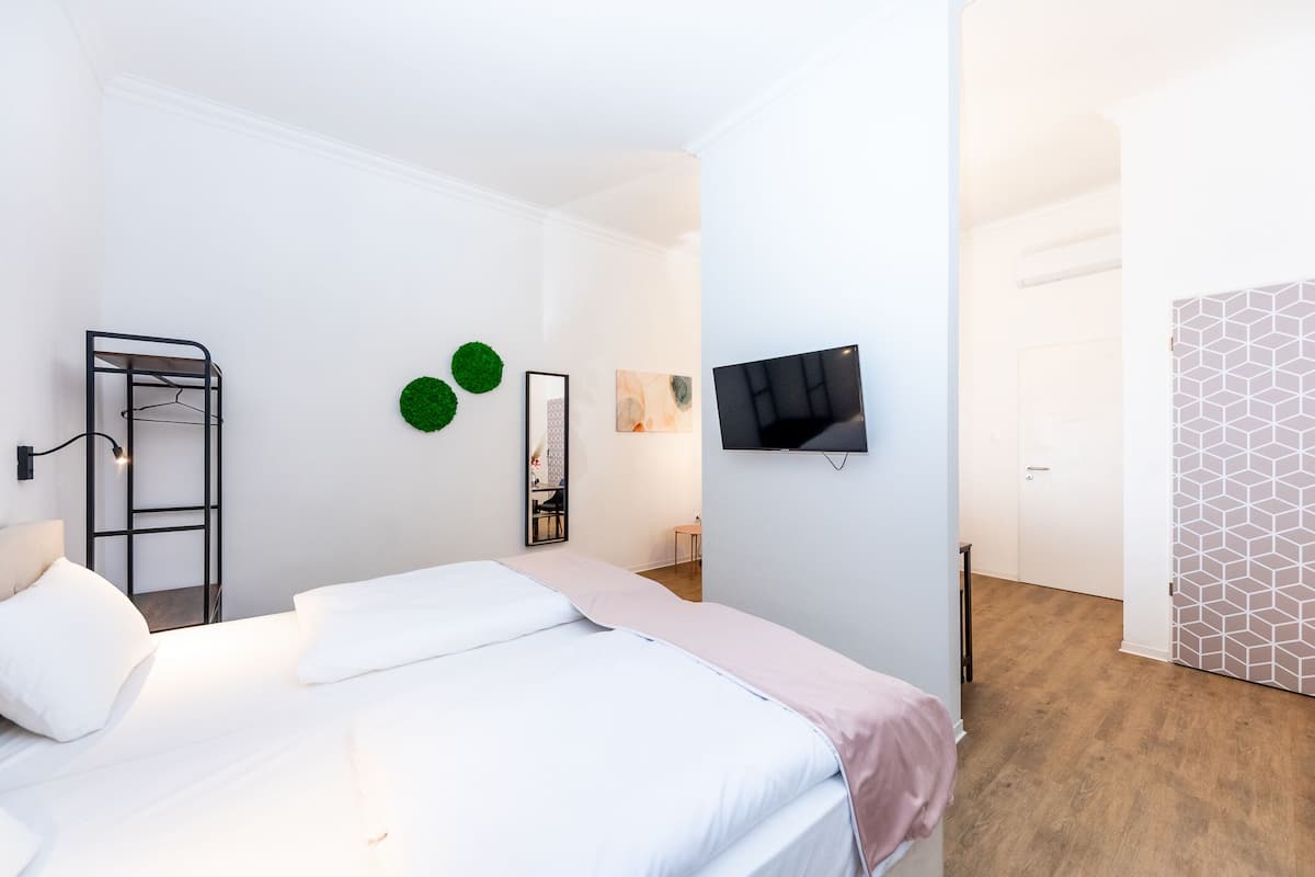 A bedroom with a bed, a TV mounted on the wall, a ladder, and a door with a geometric pattern.