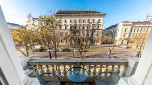 A balcony with a table and chairs, overlooking a street with buildings and trees. - Adagio Downtown Rooms (Budapest)