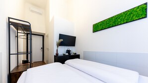 A hotel room with a bed, a desk, a chair, a television, and a green wall decoration. - Adagio Downtown Rooms (Budapest)