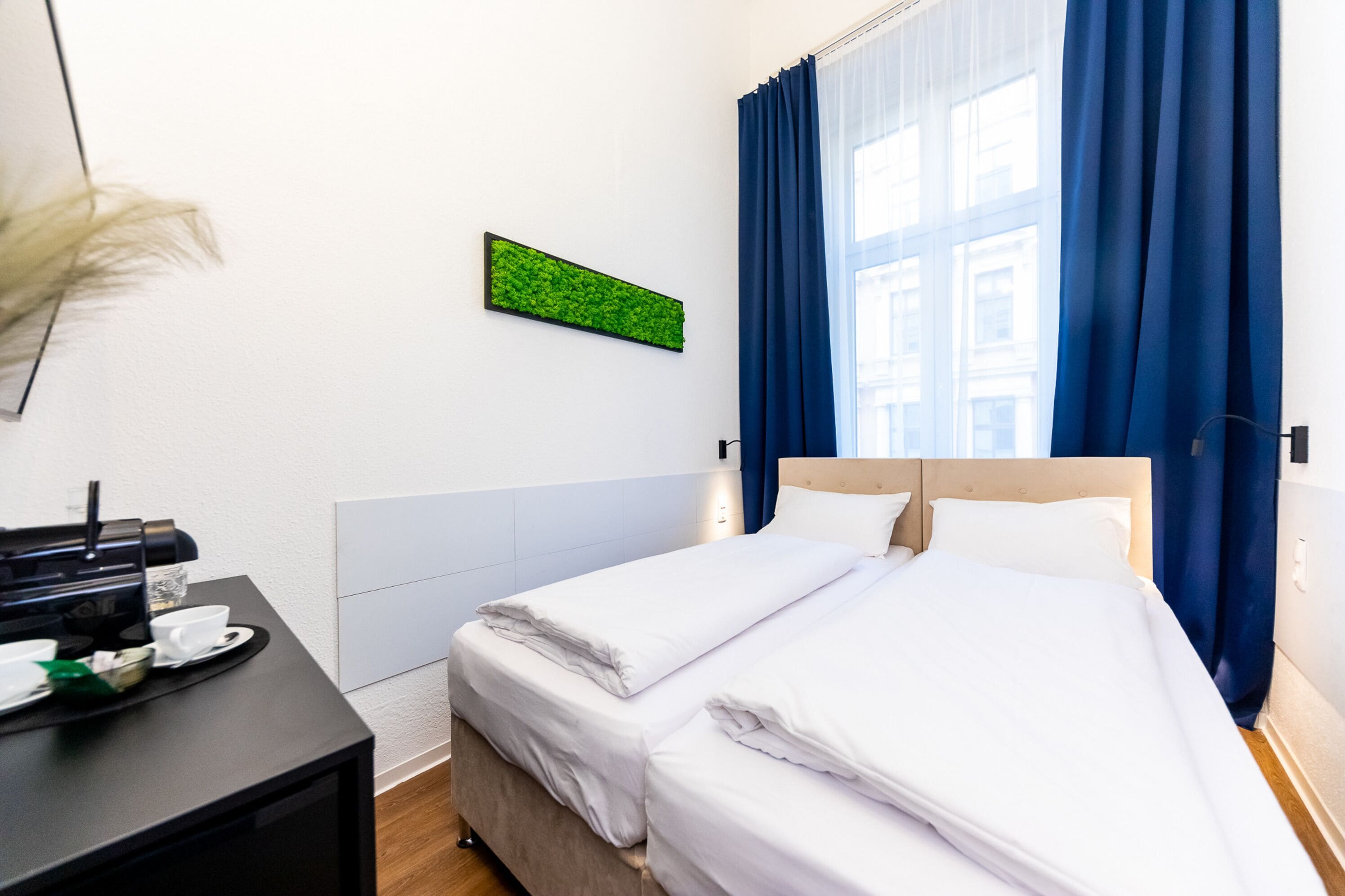 A hotel room with a bed, a coffee machine, and a wall-mounted green plant.