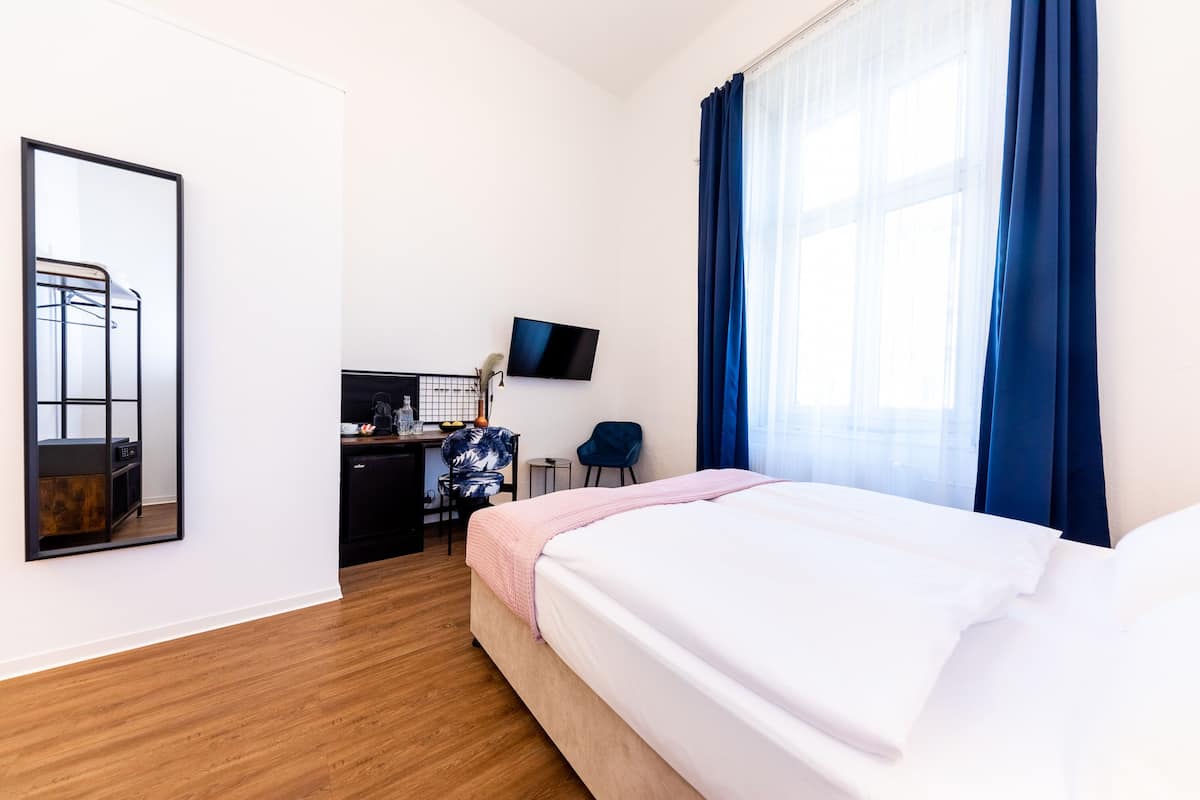 A hotel room with a bed, a desk with a computer, a chair, a TV, and a large window with curtains.