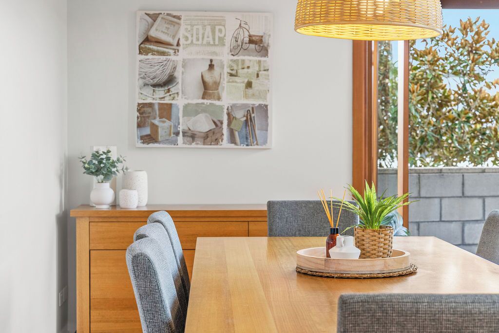 A dining area with a wooden table, grey upholstered chairs, a woven pendant light, and a wall-mounted collage of images.