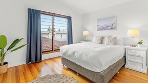 A bedroom with a large bed, two bedside tables with lamps, a window with curtains, a ceiling fan, and a wall-mounted painting. - Beach House - Lennox Head (Lennox head)