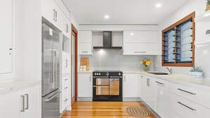 A modern kitchen with white cabinetry, a stainless steel refrigerator, a black oven, and a wooden floor.