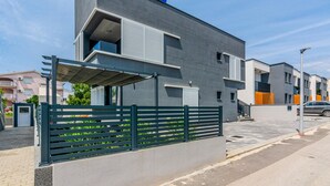 Un moderno edificio residenziale a due piani con facciata grigia, un balcone e un ingresso con cancello.