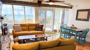 A cozy living room with a yellow sofa, a wooden coffee table, and a dining area with blue chairs.