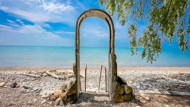 An arched stone structure on a pebbled beach with a clear view of the sea.